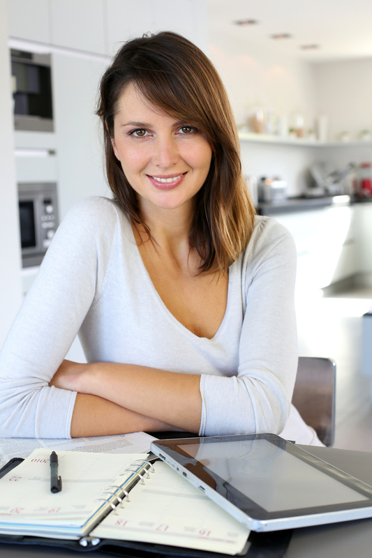 young woman sitting at a kitchen table with planner and tablet