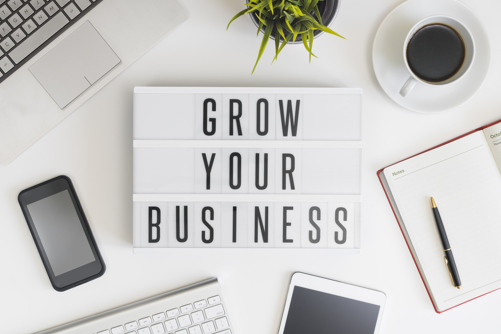 grow your business sign on desk with computer, tablet, phone, notepad and coffee