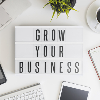 grow your business sign on desk with computer, tablet, phone, notepad and coffee